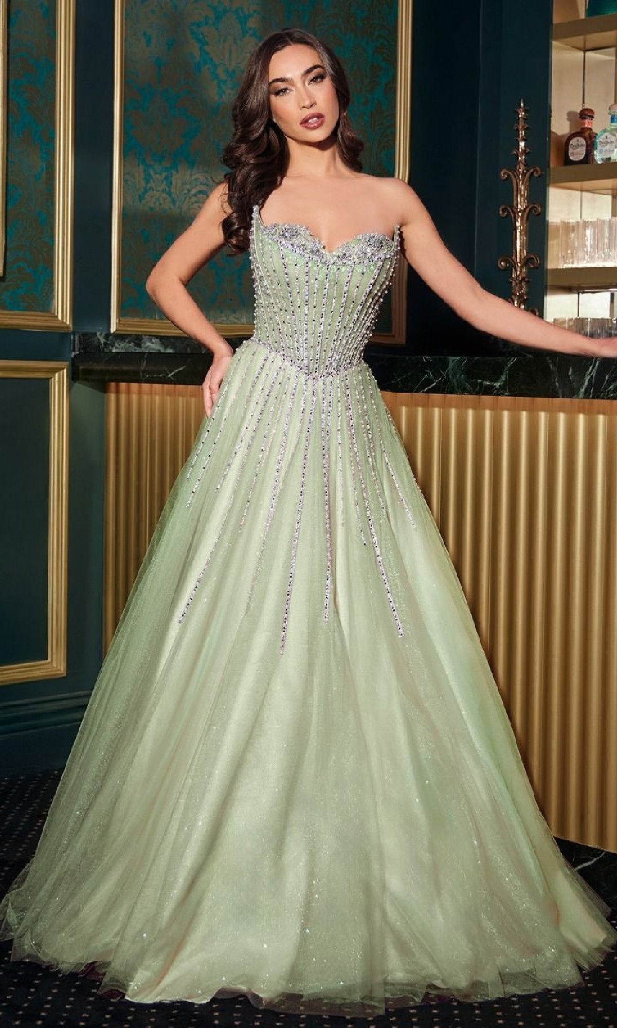 A woman stands indoors wearing the Strapless Beaded Prom Ball Gown: Ladivine CDS541—a light green dress featuring a strapless, embellished bodice and a full, sparkling skirt.